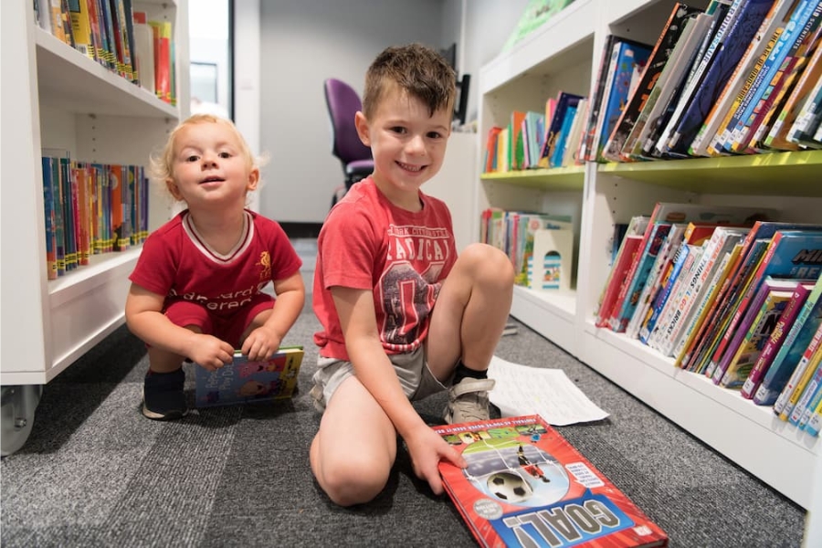 two small boys reading books on the floor in a library