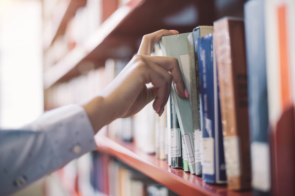 A person picking a book from a library bookshelf