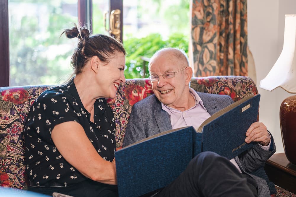 Older man reading book with carer 3x2 resize An older man reading a book with a young carer