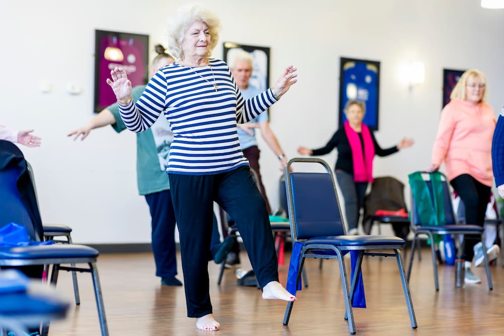 Strength and balance stock resize Group of older people stretching and balancing with chairs