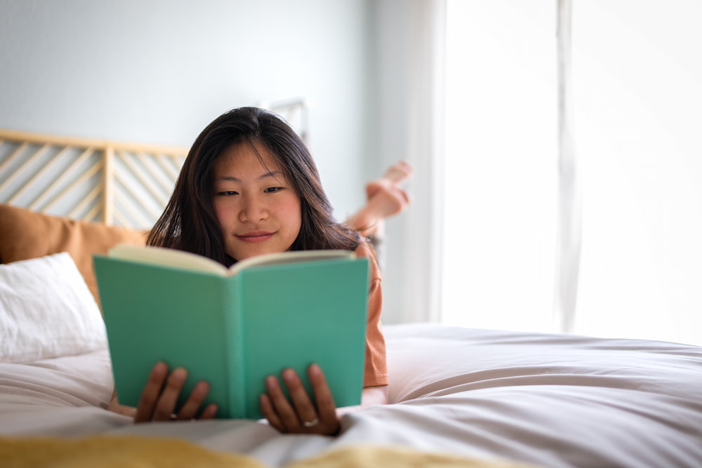 Young woman laying on a bed reading a book