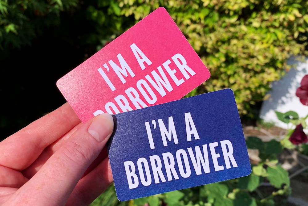 Library cards pink and blue garden edit resize Close-up of a hand holding two library cards, one pink one blue, with the words 'I'm a Borrower' on