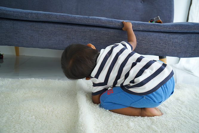 Child looking for lost book stock resize A young child looking for something under a sofa