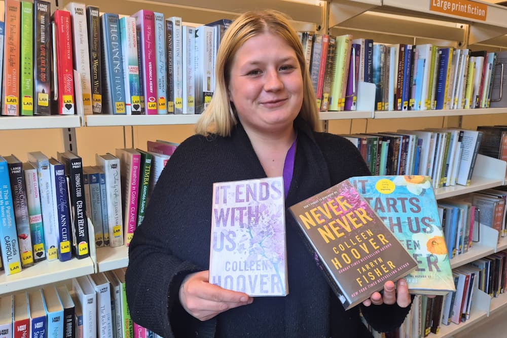 Elisha Richmond holding some of her favourite books in front of library shelves