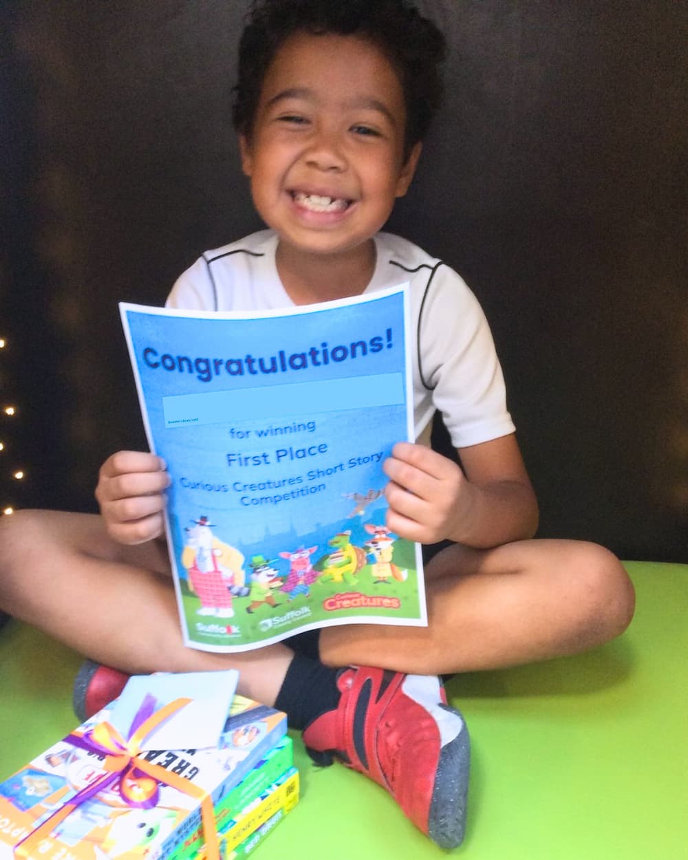 A young boy sat in a reading nook holding a winners certificate