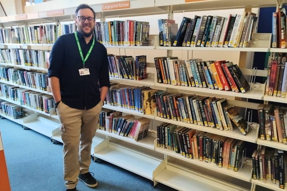 Jon HLS Volunteer standing in front of the bookshelf